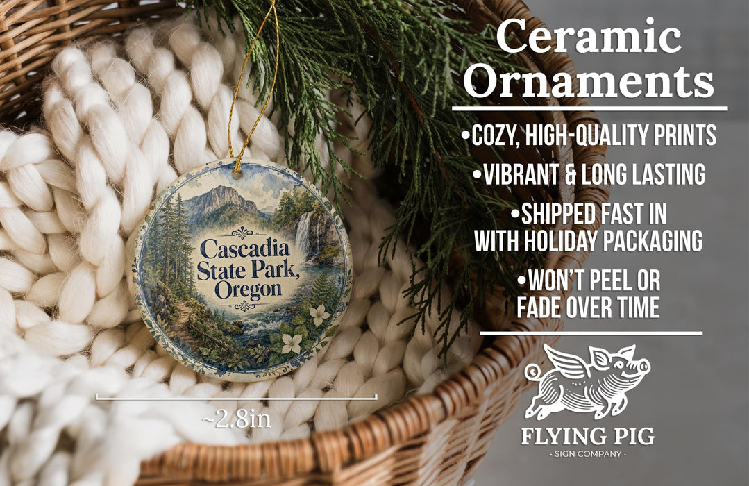 Ceramic ornaments, featuring a design of a mountain landscape with the text "Cascadia State Park, Oregon" and a bird, are displayed in a woven basket.
