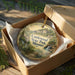 A decorative ornament in a box, featuring a scenic landscape with a waterfall and trees, with the text "Castlewood State Park, Missouri" printed on it.