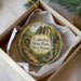 A decorative ornament in a box, featuring a scenic image of Cathedral State Park in West Virginia.