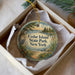 A decorative ornament in a box, featuring a scenic landscape with a lake, trees, and a bird, with the text "Cedar Island State Park, New York" printed on it.