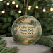 A circular ornament with a scenic landscape of a lake, trees, and a bird, hanging from a string.