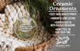 Ceramic ornaments, featuring a round ornament with a landscape scene and text, are displayed in a basket with pine branches.