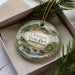A decorative ornament in a box, featuring a scenic image of Chapman State Park in Pennsylvania.