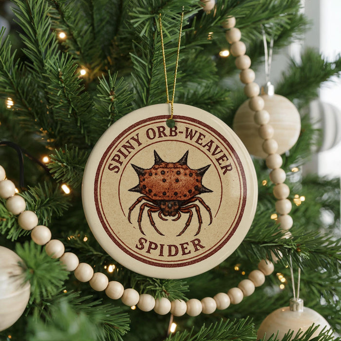 A Christmas tree decorated with ornaments, including a round ornament with a spider image and the text "SPINNY ORB-WEAVER SPIDER".
