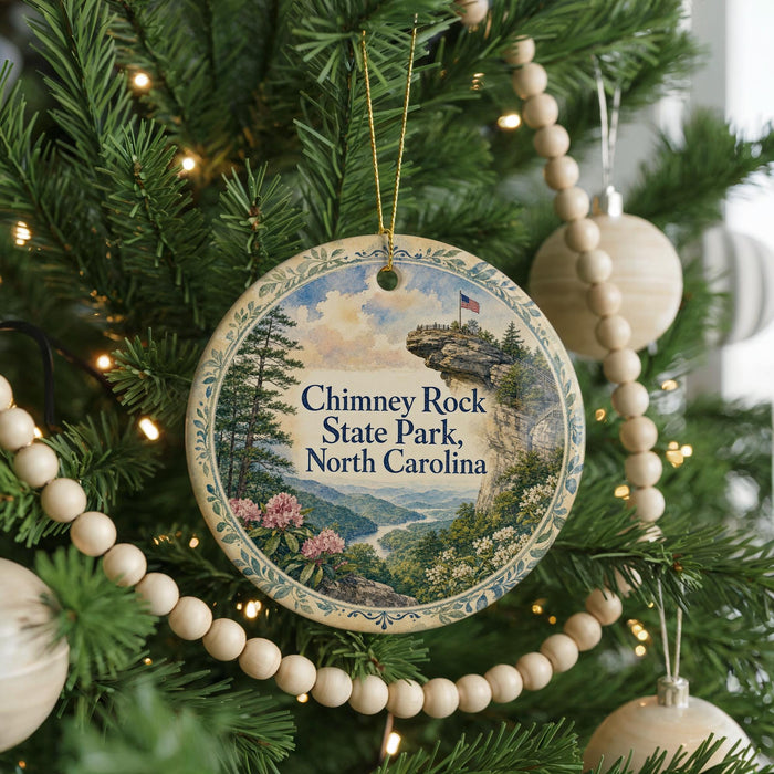 A round ornament hanging on a Christmas tree, featuring a scenic landscape with mountains, trees, and a river.