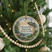 A round ornament hanging on a Christmas tree, featuring a scenic landscape with mountains, trees, and a river.