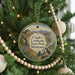 A round ornament hanging on a Christmas tree, featuring a scenic landscape with mountains, a river, and a building.