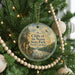 A round ornament hanging on a Christmas tree, featuring a scenic landscape with cliffs and a river.