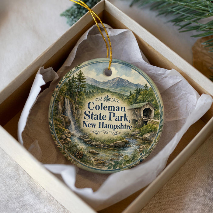 A decorative ornament in a box, featuring a scenic image of the state park in New Hampshire.