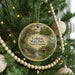 A round ornament hanging on a Christmas tree, featuring a scenic landscape with a bridge and a bird in flight.