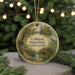 A round ornament with a painting of a park scene, featuring a bridge, trees, and a bird, hanging from a string.