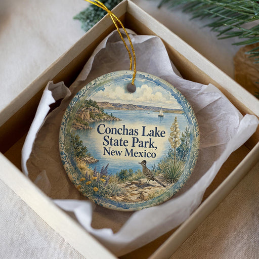 A decorative ornament in a box, featuring a scenic landscape with a lake, mountains, and a bird.