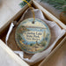 A decorative ornament in a box, featuring a scenic landscape with a lake, mountains, and a bird.
