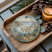 A decorative ornament with a scenic image of Conchas Lake State Park, New Mexico, is displayed on a wooden tray alongside pine cones and a lit candle.