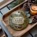 A decorative ornament featuring a scenic image of Cook Forest State Park, Pennsylvania, with a candle and pine cones on a wooden tray.