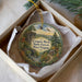A decorative ornament in a box, featuring a scenic landscape with a bridge, trees, and a mountain.