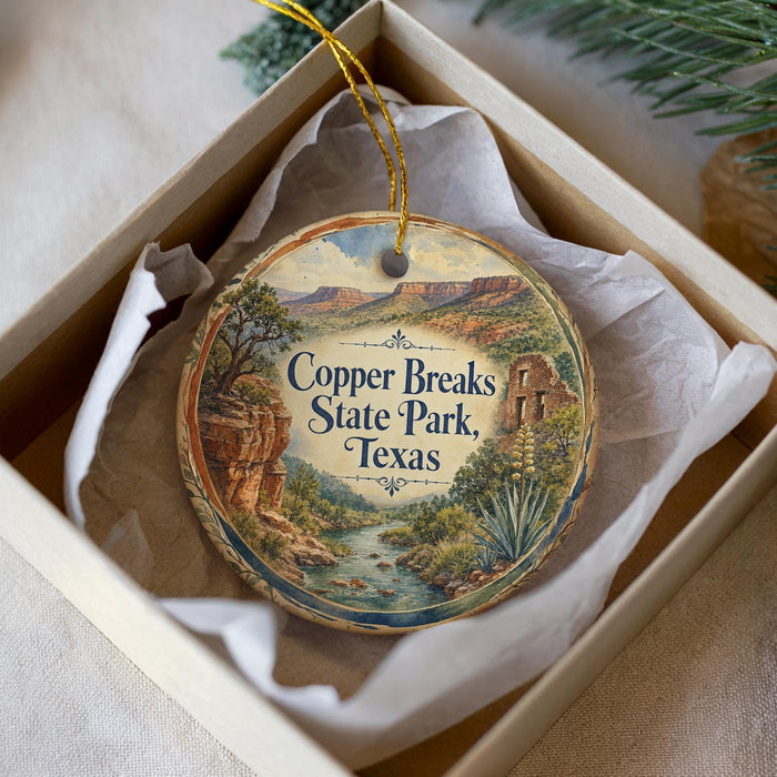 A decorative ornament in a box, featuring a scenic landscape with mountains, trees, and a river.