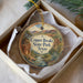 A decorative ornament in a box, featuring a scenic landscape with mountains, trees, and a river.