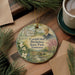 A circular ornament featuring a portrait of a man surrounded by a landscape with a house, trees, and a stream.