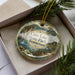 A decorative ornament with a scenic landscape of Cove Lake State Park, Tennessee, displayed in a box with pine branches.