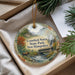 A decorative ornament with a scenic image of a bridge and a moose, surrounded by pine branches and greenery, placed in a box.