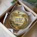 A decorative ornament in a white box, featuring a windmill, a bird, and a scenic landscape, with the text "Cross Ranch State Park, North Dakota" printed on it.
