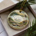 A decorative ornament in a box, featuring a scenic landscape with a river and mountains, with the text "Crowder State Park, Missouri" prominently displayed.