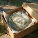 A decorative ornament in a wooden box, featuring a scenic landscape with mountains, trees, and wildlife.