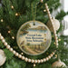 A round ornament hanging on a Christmas tree, featuring a scenic landscape with a lake, mountains, and a bird.