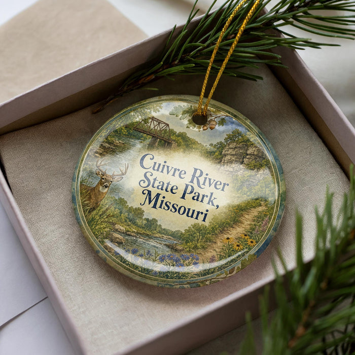 A decorative ornament in a box, featuring a scenic landscape with a river, bridge, and wildlife.
