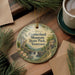 A decorative ornament featuring a scenic landscape with a waterfall, surrounded by pine branches and a cup of coffee on a wooden surface.