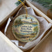 A decorative ornament in a box, featuring a scenic landscape with a lake, mountains, and a bird in flight.