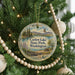 A round ornament hanging on a Christmas tree, featuring a scenic landscape with a lake, mountains, and a bird in flight.