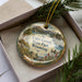 A decorative ornament in a box, featuring a scenic landscape with mountains, trees, and wildlife, including a duck.