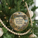 A round ornament hanging on a Christmas tree, featuring a scenic landscape with mountains, a river, and a goat.