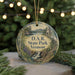 A round ornament with a scenic landscape of D.A.R. State Park, Vermont, featuring a waterfall and a castle, is displayed on a table with Christmas lights in the background.