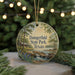 A round ornament with a painting of Daingerfield State Park in Texas, featuring a cabin and a river, is displayed in front of a blurred background with Christmas lights.