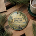 A decorative ornament with a scenic landscape of Dash Point State Park in Washington, featuring pine trees, a lake, and a bird in flight.
