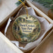 A decorative ornament in a box, featuring a scenic landscape with a waterfall and pine trees, with the text "David Crockett State Park, Tennessee" printed on it.