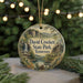 A round ornament with a scenic landscape of David Crockett State Park in Tennessee, featuring a waterfall and pine trees, is displayed on a table with Christmas lights in the background.
