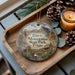 A wooden tray with a decorative ornament featuring a scenic landscape of Davis Mountains State Park, Texas, along with pine cones and a lit candle.