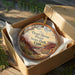 A decorative ornament in a cardboard box, featuring a scenic image of Dead Horse Point State Park in Utah.