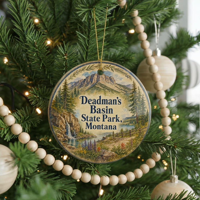 A round ornament hanging on a Christmas tree, featuring a scenic landscape with mountains, a waterfall, and pine trees.