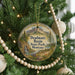 A round ornament hanging on a Christmas tree, featuring a scenic landscape with mountains, a waterfall, and pine trees.