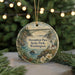 A decorative ornament featuring a scenic landscape with a bridge, lighthouse, and water, hanging from a string.