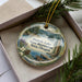 A decorative ornament with a scenic lake landscape and pine trees, featuring the text "Detroit Lake State Recreation Area, Oregon" on it.