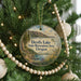 A round ornament hanging on a Christmas tree, featuring a scenic landscape with a lake and mountains.