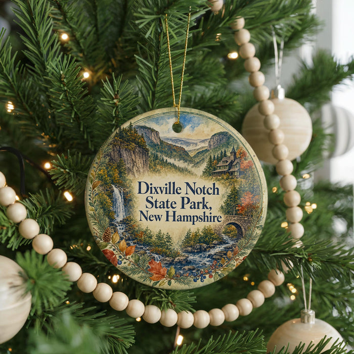 A round ornament hanging on a Christmas tree, featuring a scenic landscape with a waterfall and mountains.