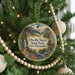 A round ornament hanging on a Christmas tree, featuring a scenic landscape with a waterfall and mountains.