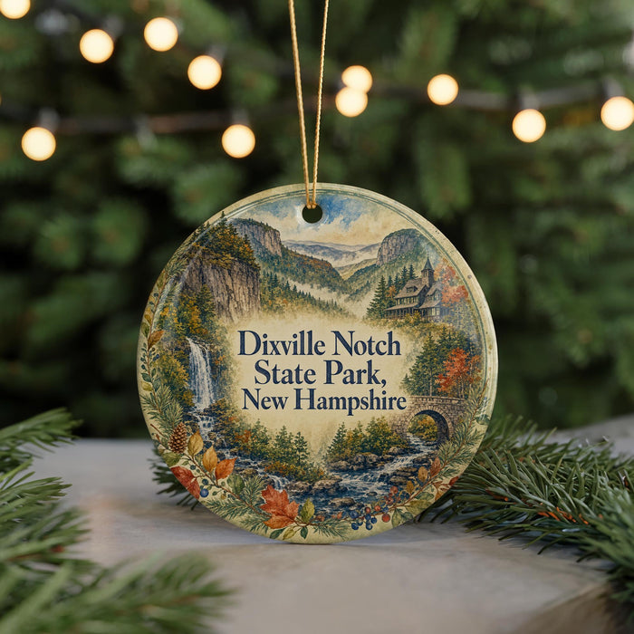 A decorative ornament featuring a scenic landscape with a waterfall, mountains, and pine trees, hanging on a string.